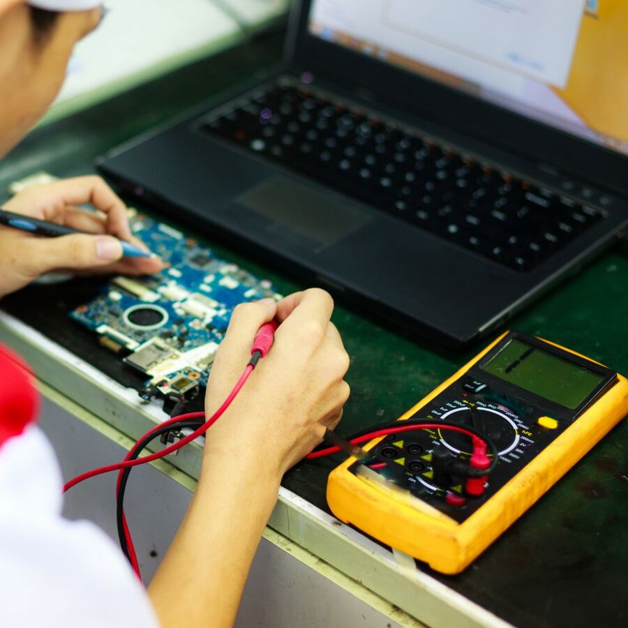 Technician diagnosing a laptop board with a multimeter